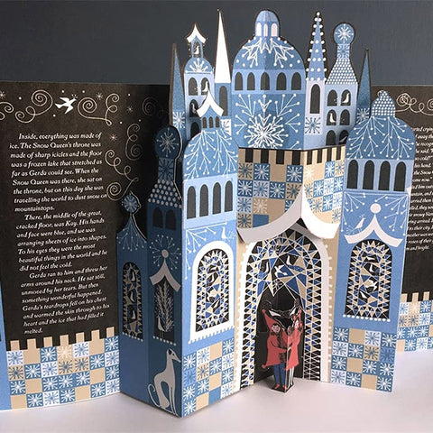 A 3D pop-up cardboard book about Santa Claus and the North Pole, featuring a detailed blue and white snowy cathedral pop-up, with text panels on the left and right on a dark background.