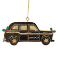 A London cab Christmas ornament shaped like a black taxi with gold glitter details, green holly leaves, red berries, and the word 'LONDON' on the side, hanging from a gold string.