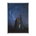 A rectangular magnet featuring a stone tower under a swirling blue night sky with star trails