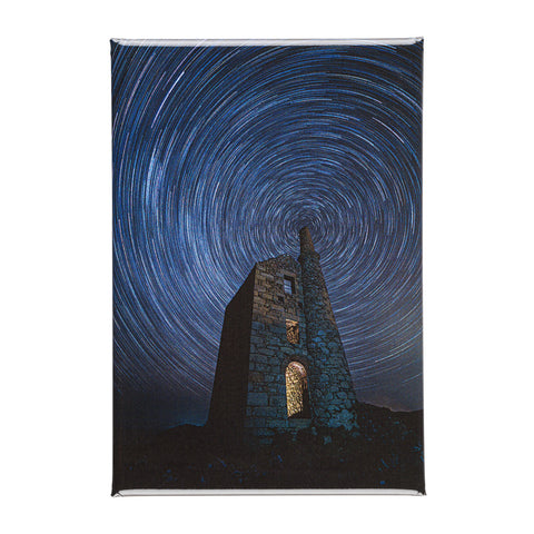 A rectangular magnet featuring a stone tower under a swirling blue night sky with star trails