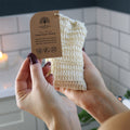 Person holding a natural soap saver pouch with a label in a bathroom setting