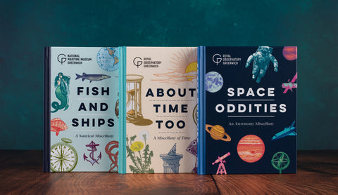 Three hardcover books from National Maritime Museum Greenwich are displayed side-by-side on a wooden surface against a dark teal background. The books are titled 'Fish and Ships', 'About Time Too', and 'Space Oddities'.