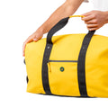 A bright yellow duffel bag with black handles and trim, being held by a person's hands
