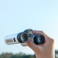 Hand holding ZWO Seestar Binoculars against a blue sky