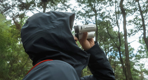 Side profile of a person outdoors in a forest holding the ZWO Seestar Binoculars up to their eyes