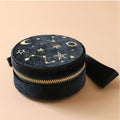 Round black pouch with star and moon designs and gold zipper on a beige background