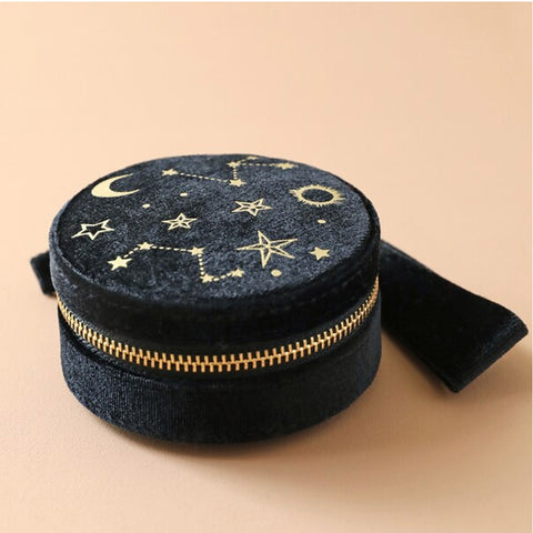 Round black pouch with star and moon designs and gold zipper on a beige background
