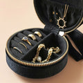 Black jewelry case with gold rings and necklaces on a beige background