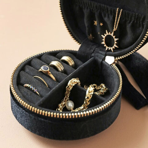 Black jewelry case with gold rings and necklaces on a beige background