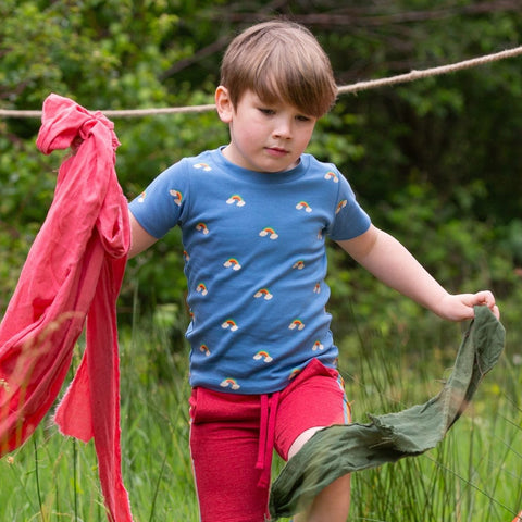 Child wearing a blue t-shirt with repeating pattern of rainbows with clouds