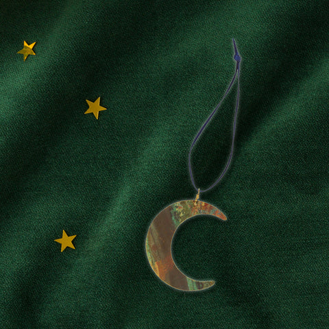 Moon-shaped brass decoration on a green fabric background with gold stars