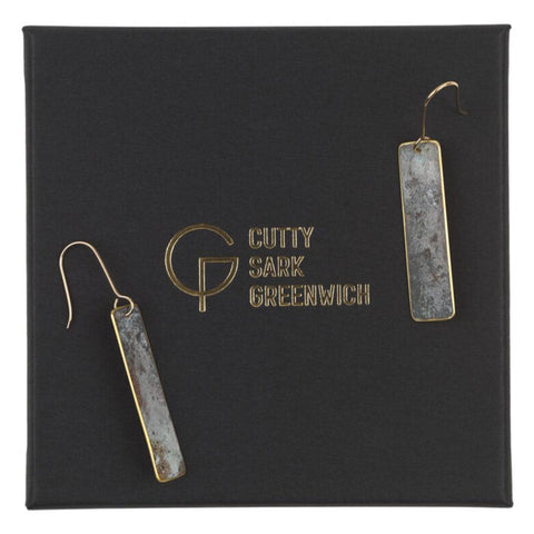 Two tarnished brass earrings with gold wire hooks on a black box with gold writing.