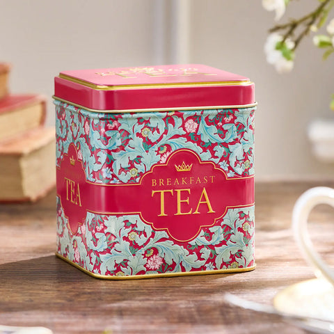 Red tin of breakfast teabags on a wooden surface with a teacup