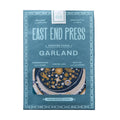 East End Press Garland printed paper in a dusty blue box, featuring a window that shows a patterned navy and gold garland, with text highlighting its handcrafted and recycled qualities.