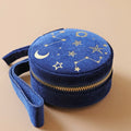 Round navy fabric jewellery holder with a gold zip and gold constellation design, against a peach background.