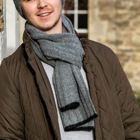 Person wearing grey ribbed scarf with black trim.