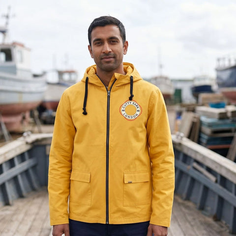 Man wearing a yellow jacket with a logo standing on a dock with boats in the background