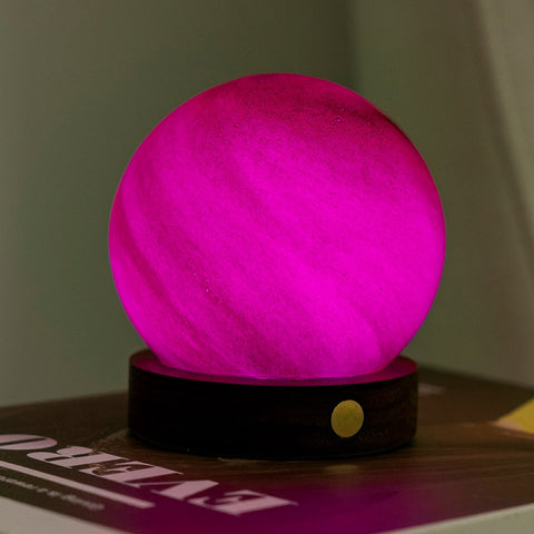 Pink spherical lamp on a wooden base with a blurred magazine in the background