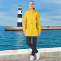 Person wearing a yellow raincoat standing by a lighthouse and body of water