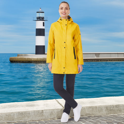 Person wearing a yellow raincoat standing by a lighthouse and body of water