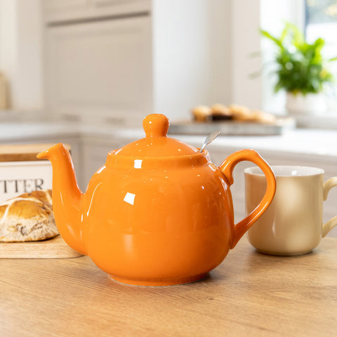 Orange teapot on a table with mug and hot cross bun.