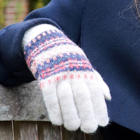 Person wearing cream gloves with pink, coral and blue Fair Isle design.