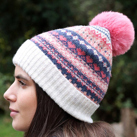 Person wearing cream, navy, pink and coal knitted hat with large pink pompom.