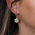 Close-up of a person wearing a gold earring with colorful beads.