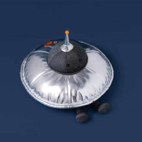 silver flying saucer plush toy with grey textured face and legs on a navy background
