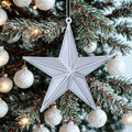 Silver star ornament hanging on a Christmas tree with white ornaments.