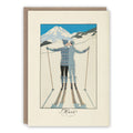 A vintage-style illustrated greeting card with a kraft envelope behind it. The card shows two skiers seen from behind in a snowy mountain landscape
