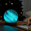 Blue glowing spherical lamp on a wooden surface with blurred Christmas tree in the background