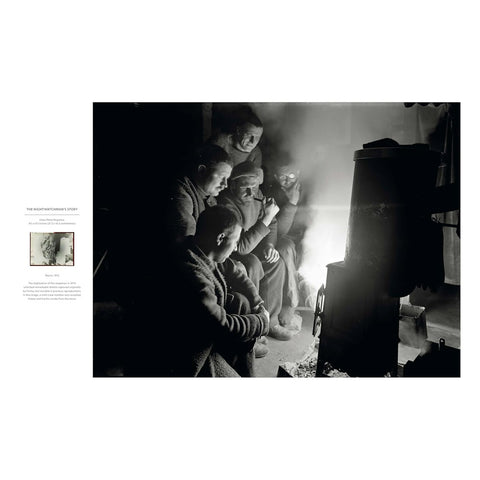 A black and white photographic print featuring a group of people gathered around a stove or heater in a dim interior, shown within a white page layout that includes a small caption and inset image on the left.