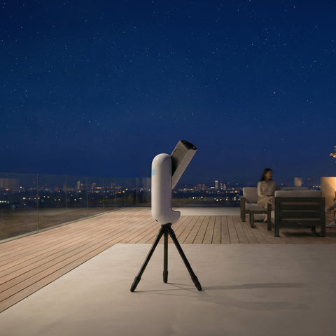 Telescope on a tripod with a person sitting on a rooftop at night, looking at the stars.
