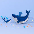 Toy whale with a smaller whale and colorful confetti on a blue background