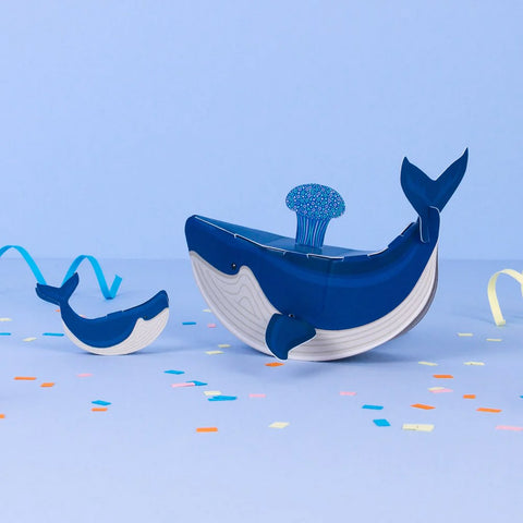 Toy whale with a smaller whale and colorful confetti on a blue background