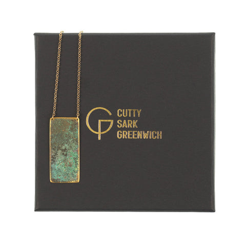 Tarnished brass rectangle with gold fine link chain on a black box with gold writing.