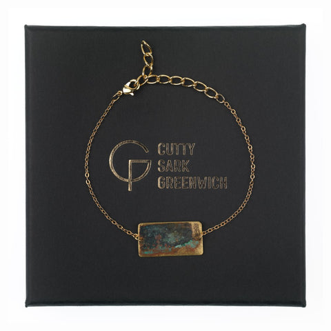 Gold chain bracelet with tarnished brass rectangle on a black box with gold writing.