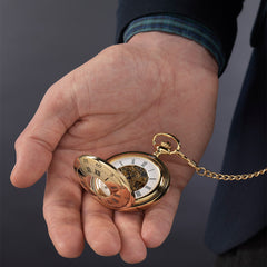 Gold finish pocket watch being held in a man's hand.