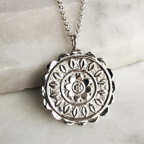 Silver pendant with embossed flower pattern.