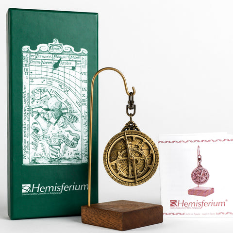 Small brass Astrolabe Astrolabio hanging from stand next to green box with renaissance style illustration